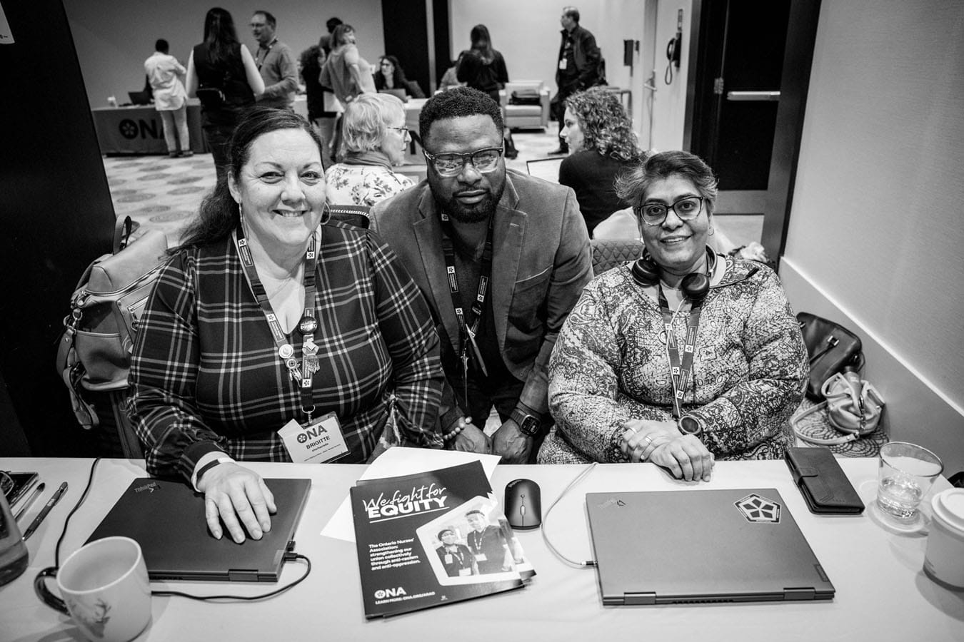 Anti-Racism and Anti-Oppression Specialists Brigitte Goar, Patrick Mazambi and Anuradha Lokre sit at table full of handouts.