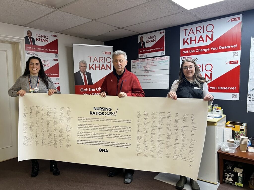 Members and candidate hold life-sized banner full of signatures.