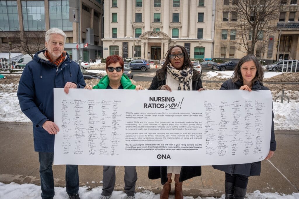 Members and candidate hold life-sized banner full of signatures.