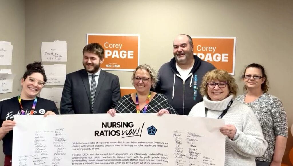 Members and candidate hold life-sized banner full of signatures.