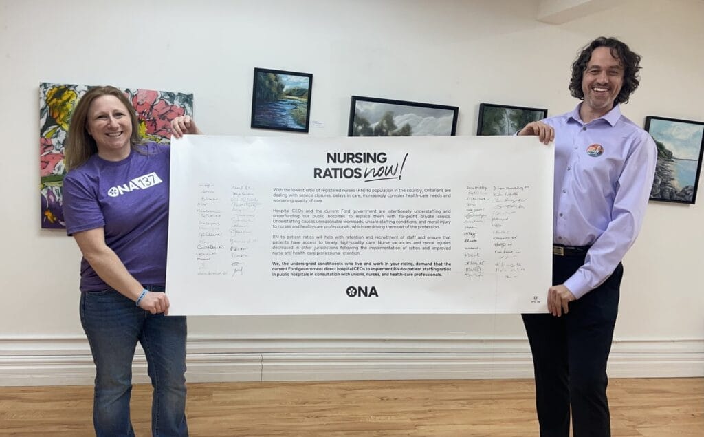 Member and candidate hold life-sized banner full of signatures in room of paintings.