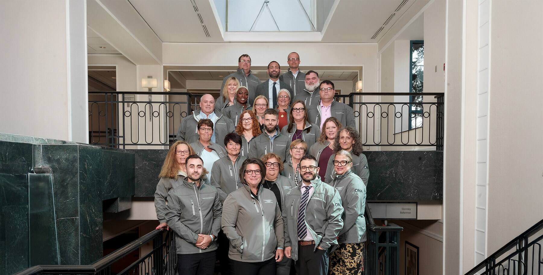 ONA Provincial President Erin Ariss and Hospital Provincial Negotiating Team Chair Jason Dupras stand on stairs with other team members, Board members and staff.