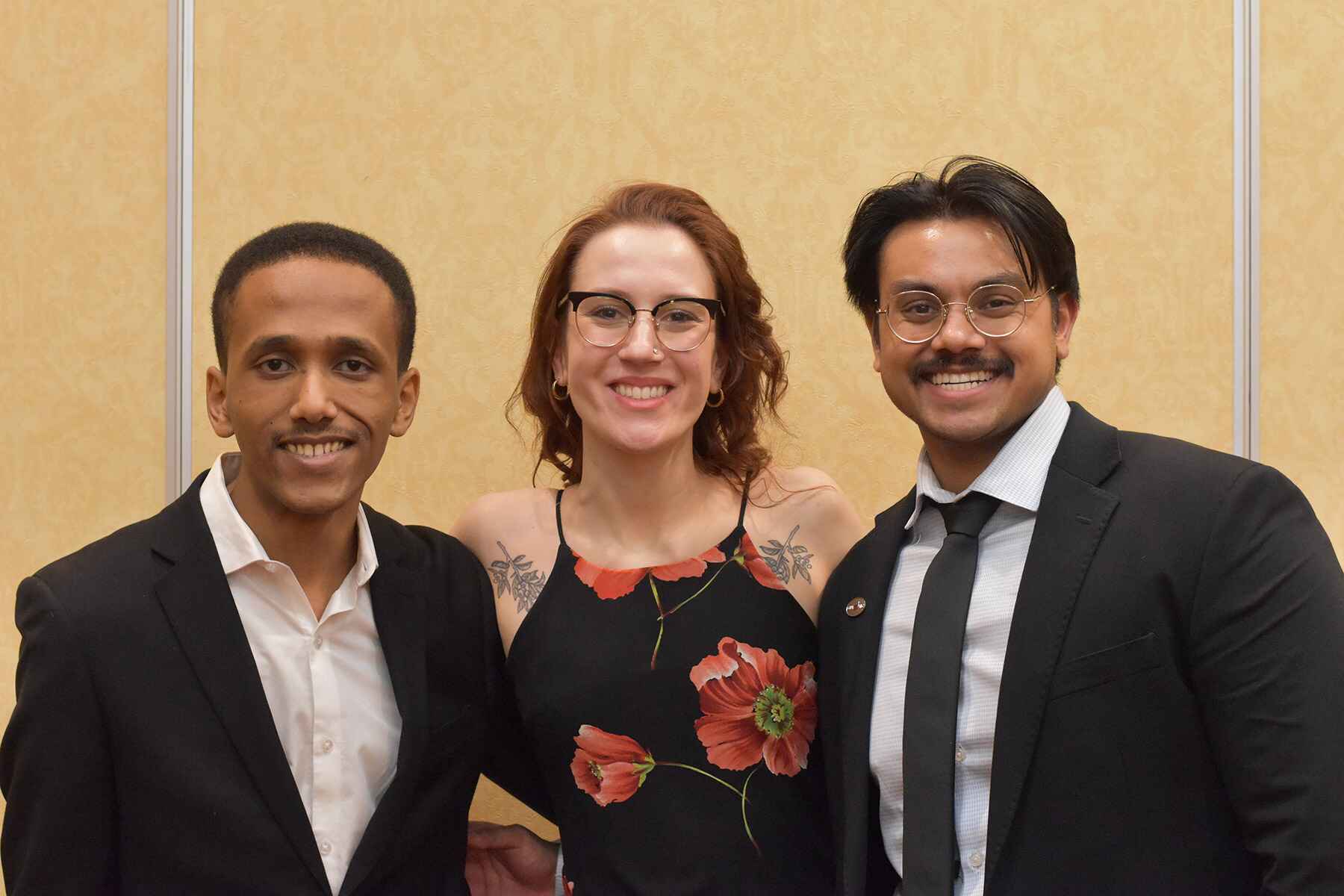 Three students stand in a row and smile.