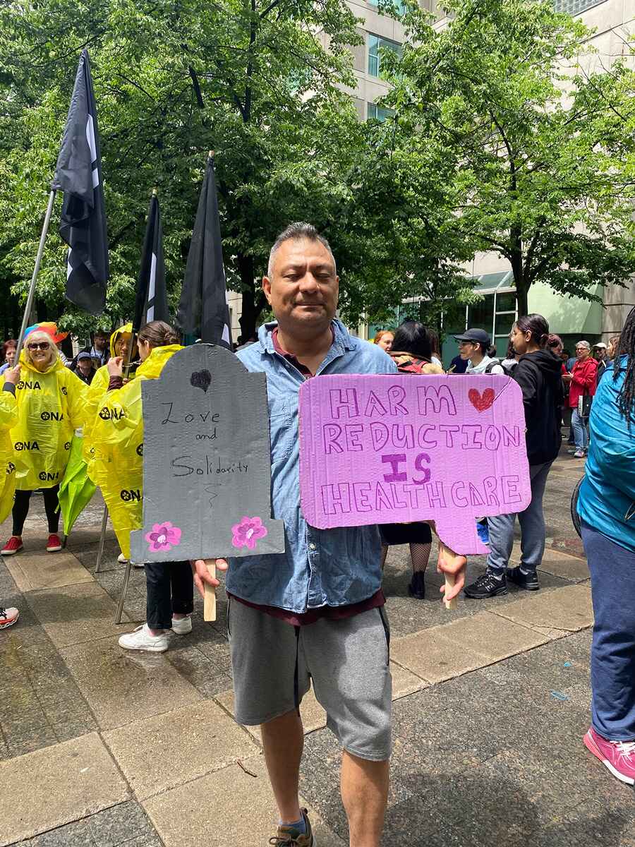 Man stands at rally holding two signs.