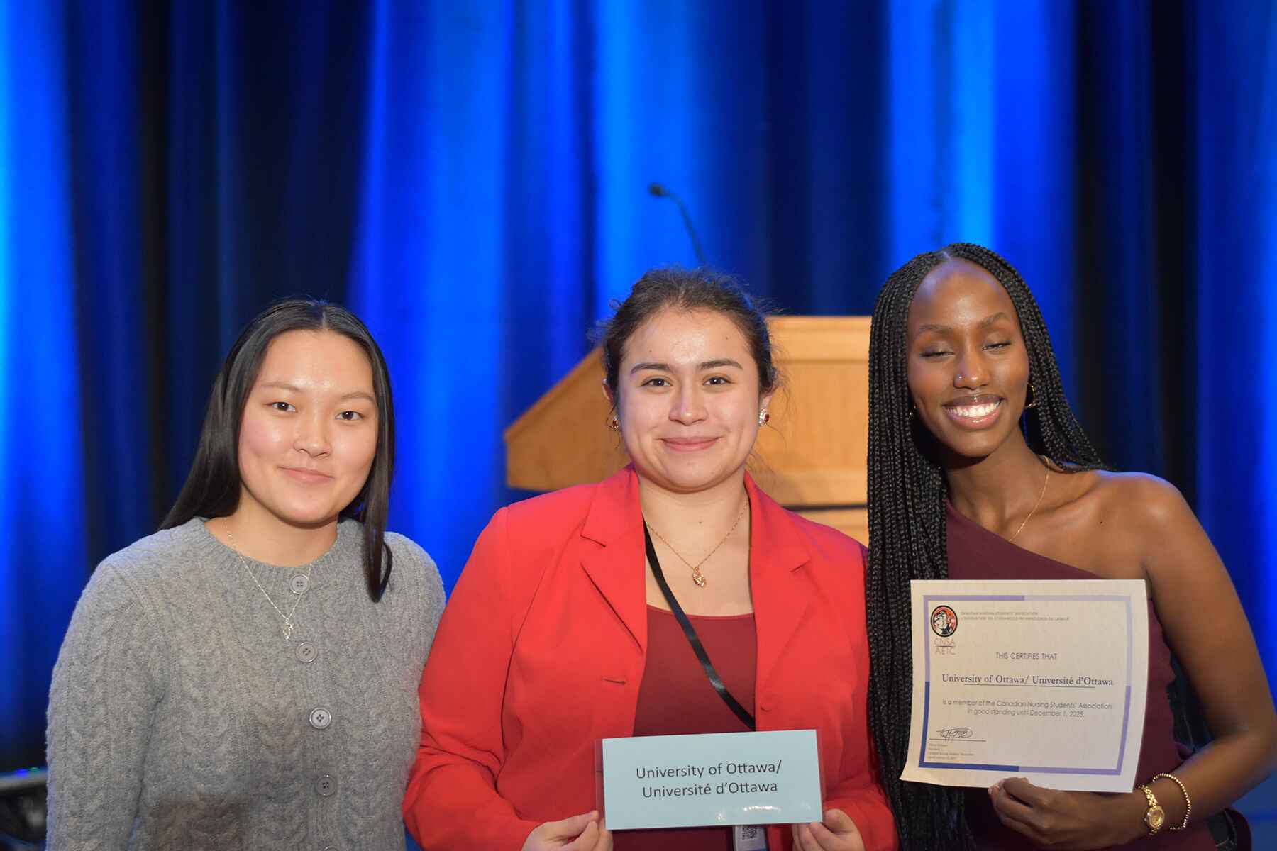 Three students, one of whom holds a certificate, smile.