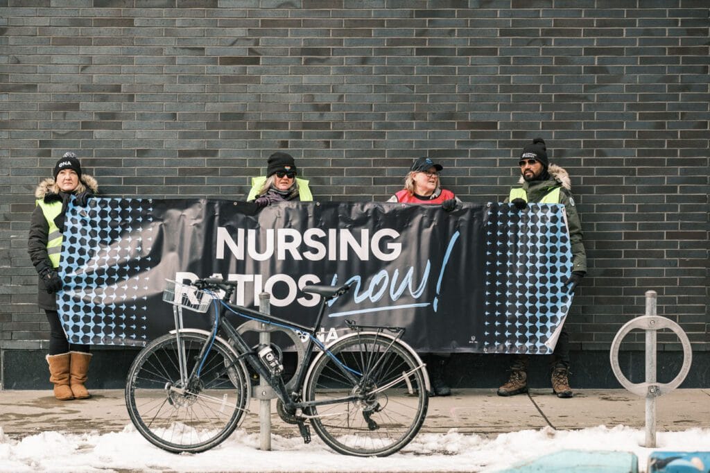 Four members stand against wall displaying large banner.