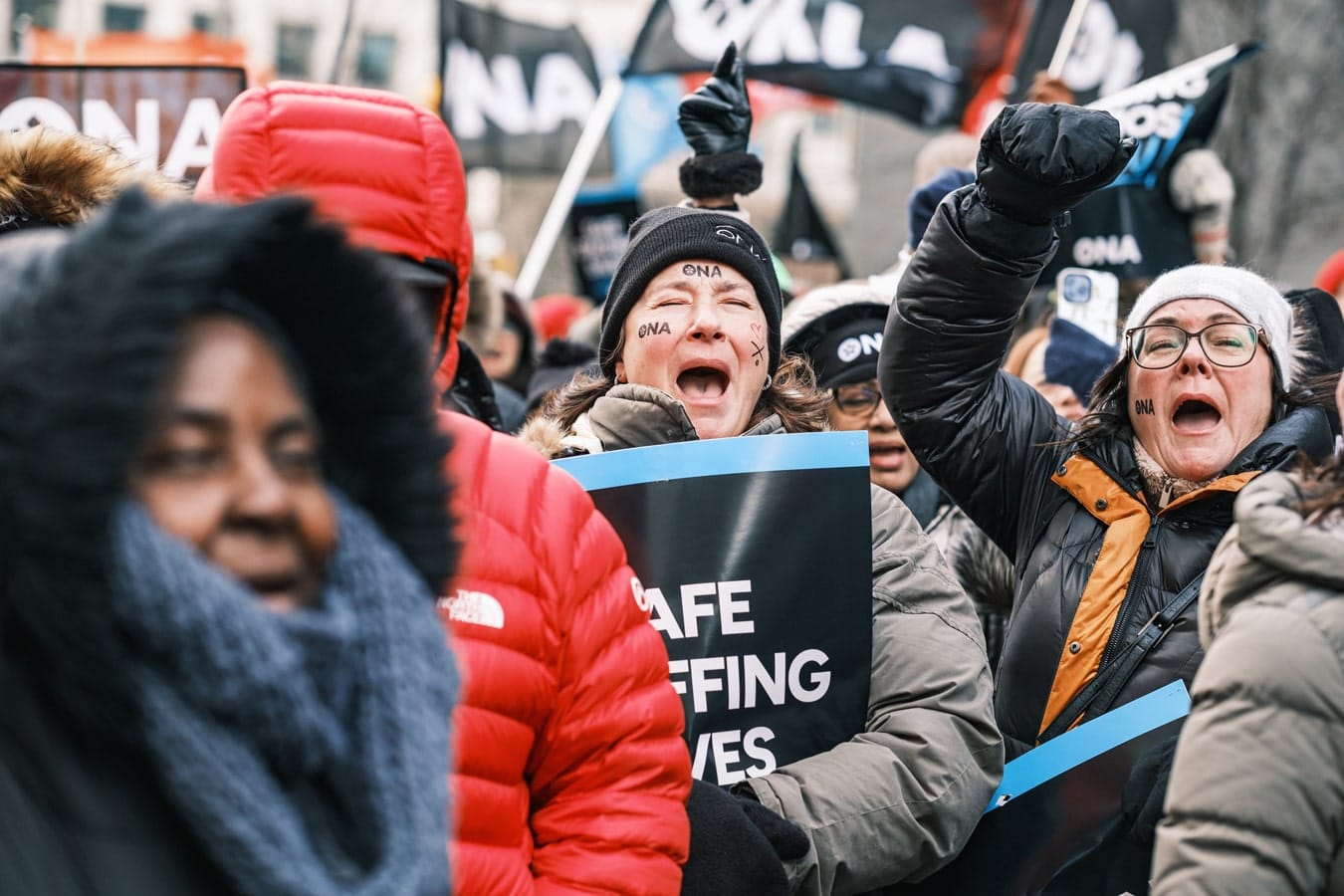 Two members, surrounded by others, shout at rally with one fist pumping.