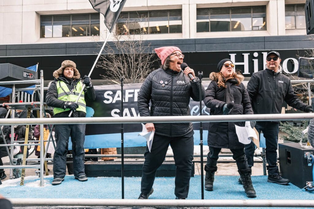 Three Board members stand on flatbed truck, with ONA Provincial President Erin Ariss shouting into a microphone.