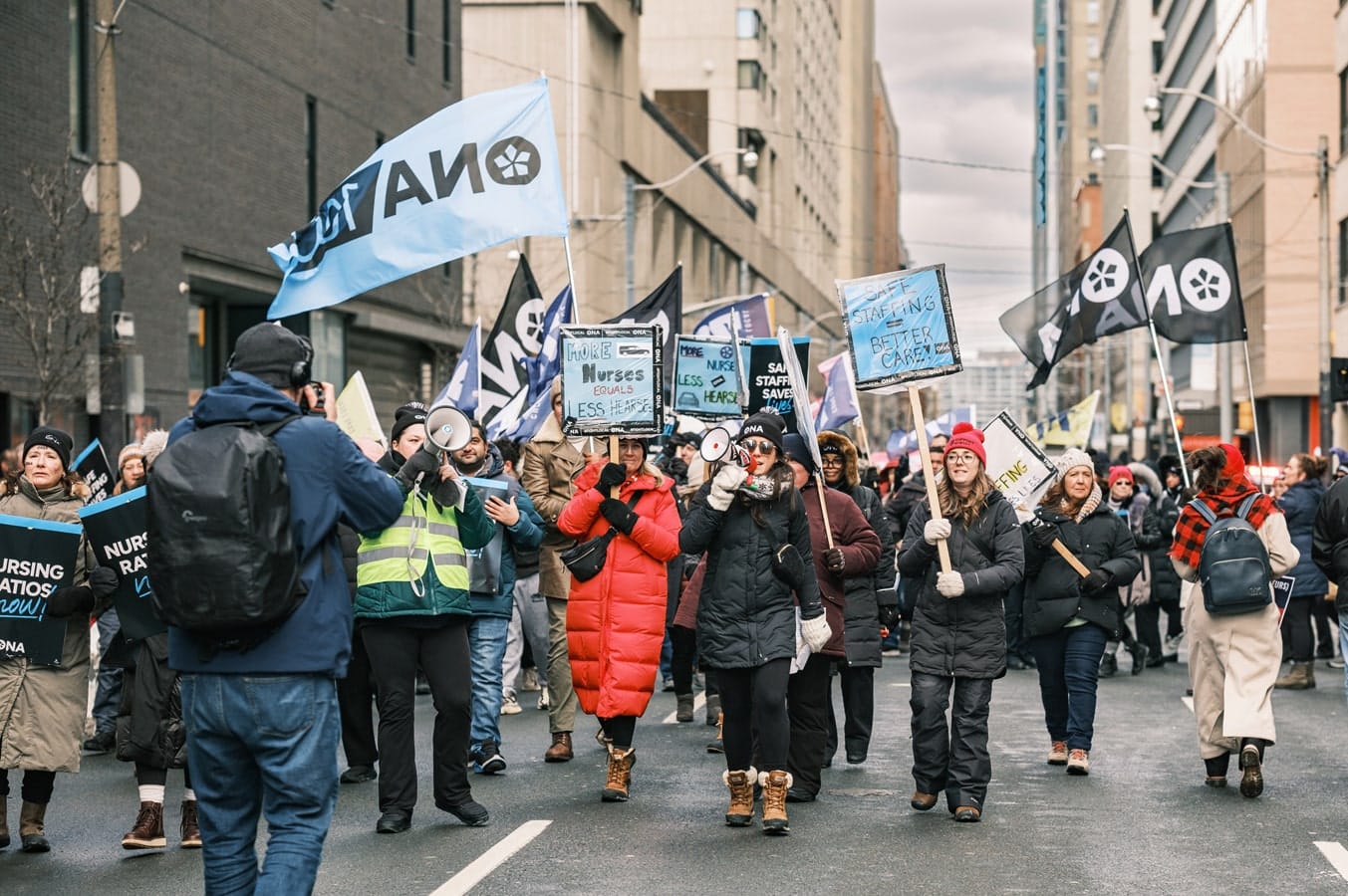 Large group marches on street, with one shouting into a megaphone.