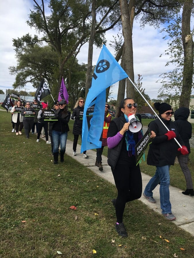 Members walk the sidewalk carrying flags and signs.