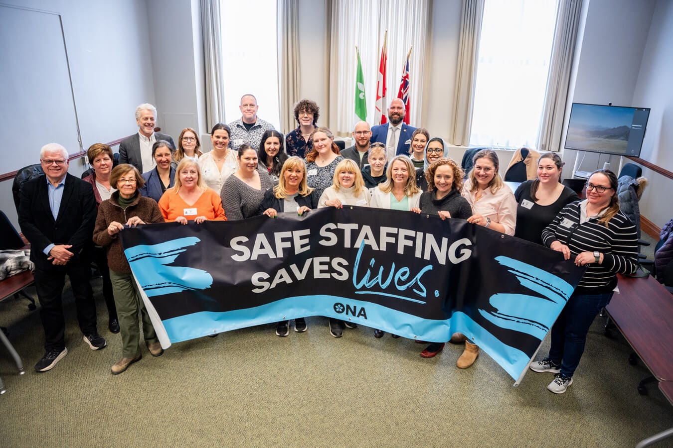 ONA secondees, including Alison Tuzi, stand behind a banner with Ontario NDP Caucus members.