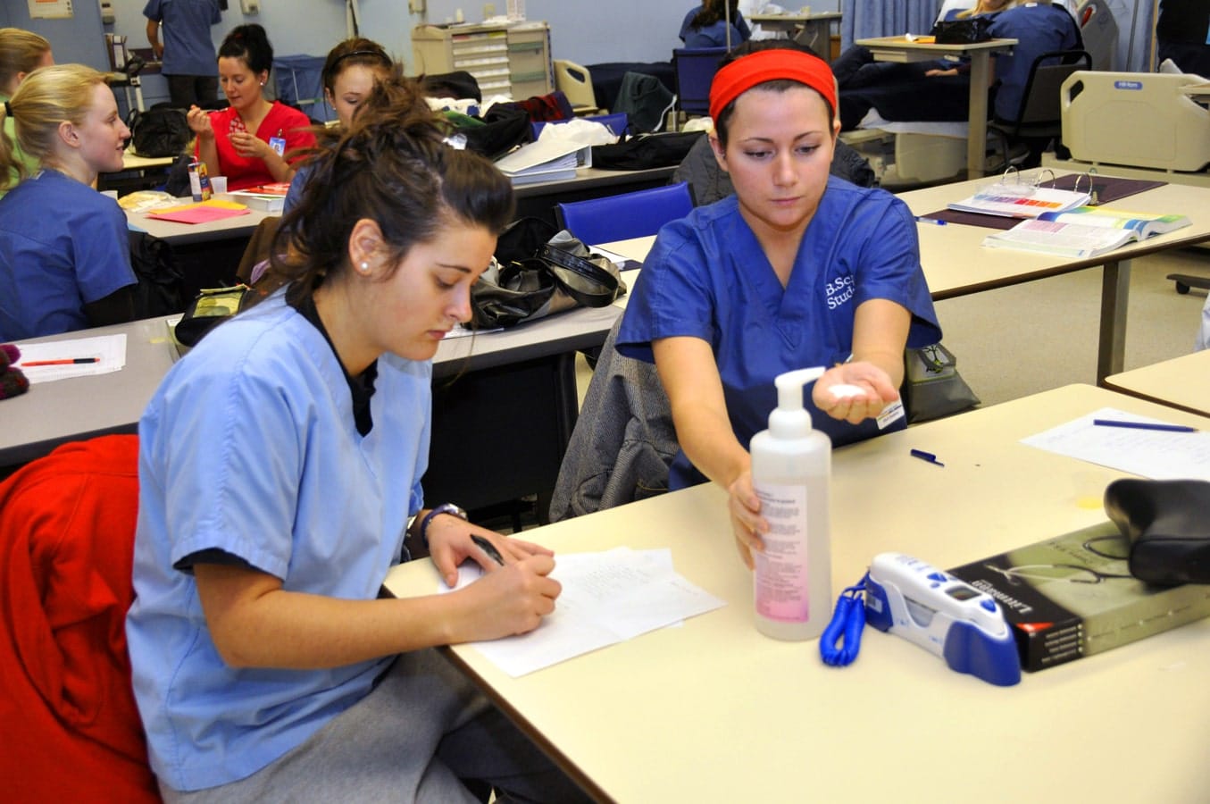 Nursing student writes on paper as another takes soap from dispenser