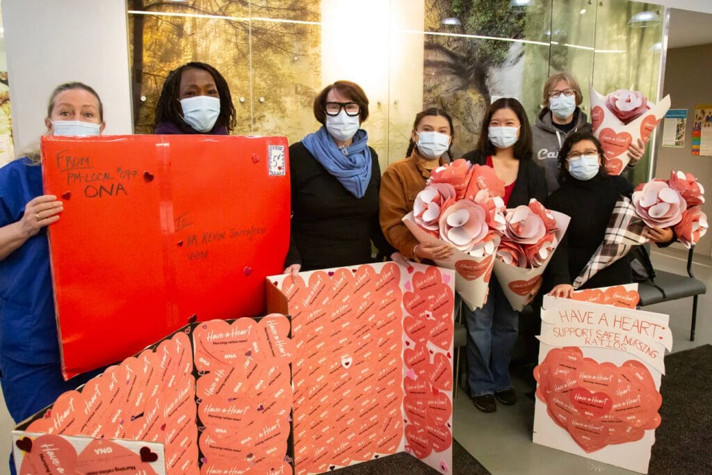 ONA97 Local Coordinator Liz Romano and members in masks hold dozens of valentines and a life-sized envelope.