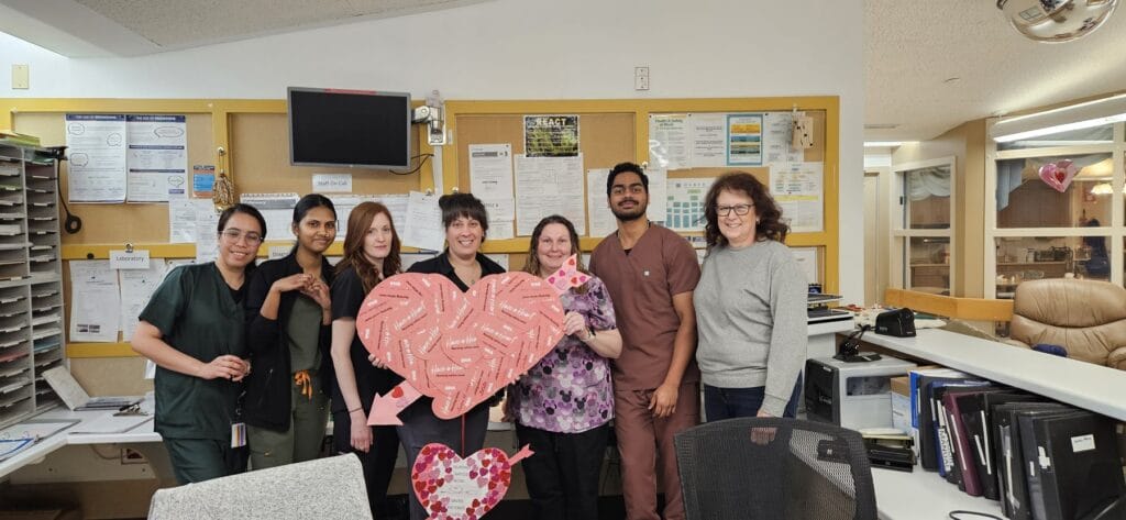 Members stand in a row holding life-sized valentines.