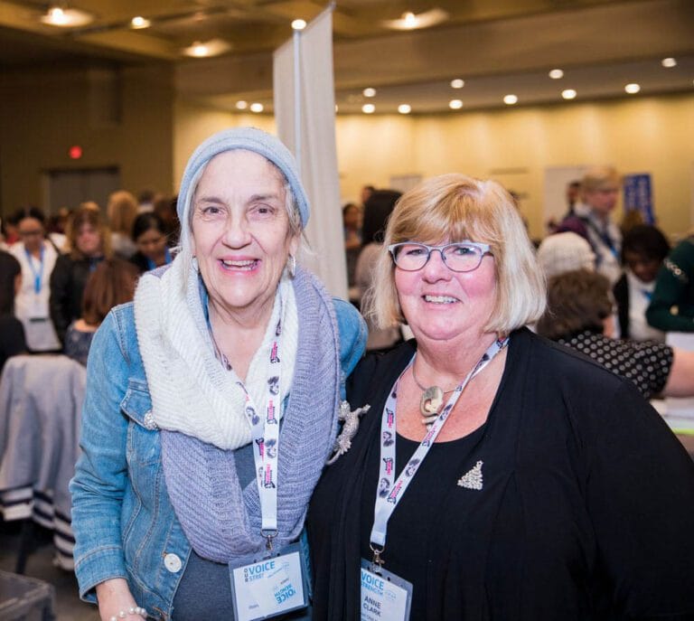 Retirees Carolyn Edgar and Anne Clark with arms around each other smile at camera.