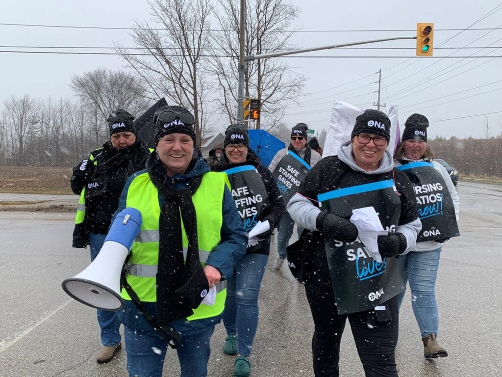 Group of smiling members walk across the street in snow towards camera.