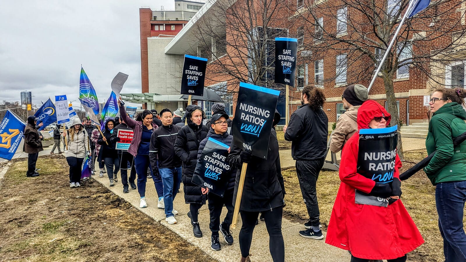 Members and union allies walk on sidewalk outside of hospital holding signs.
