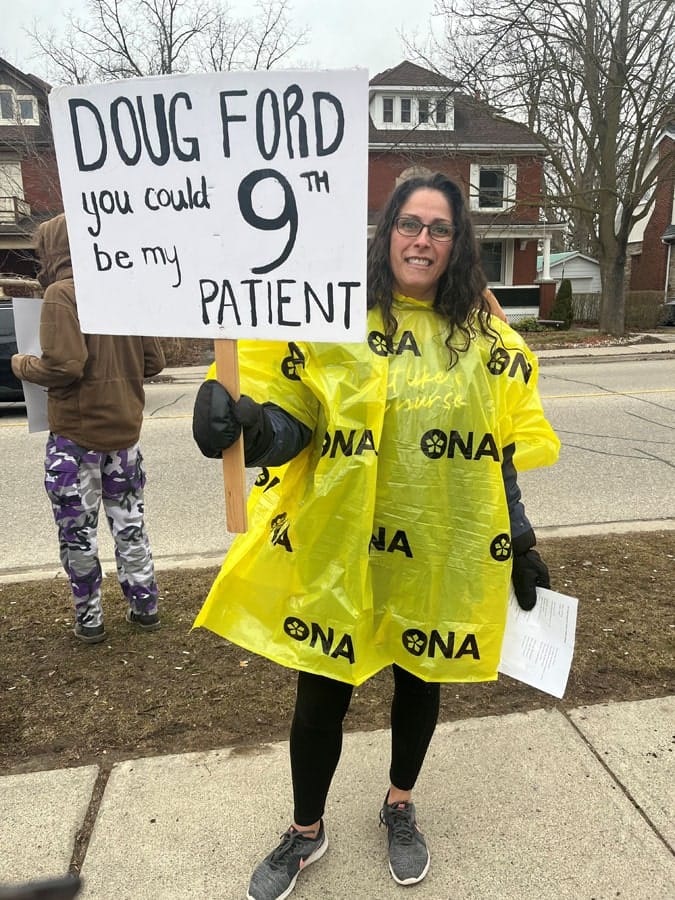 Member in yellow poncho holds handmade sign.