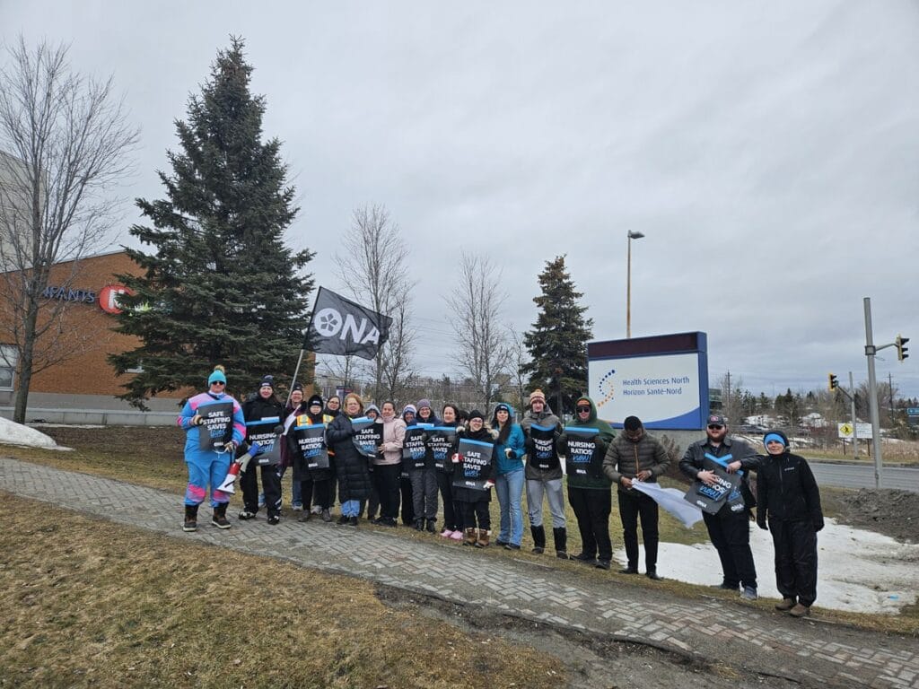 Members standing in a line hold the same signs in front of hospital’s main sign.