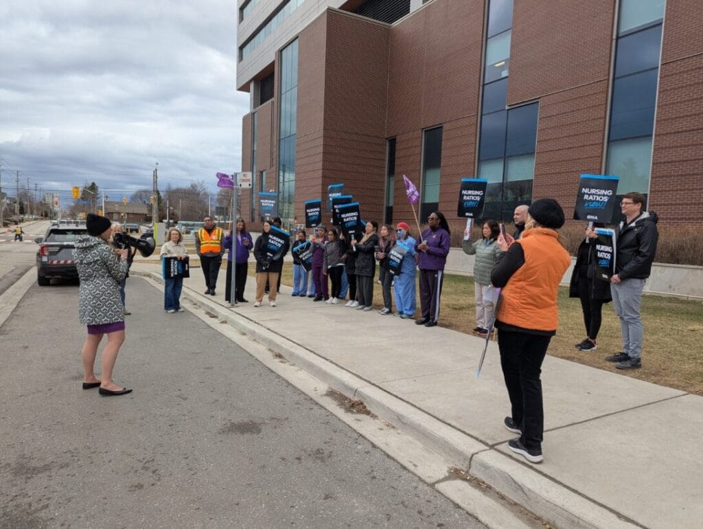 Member speaks to other members with megaphone in front of hospital.