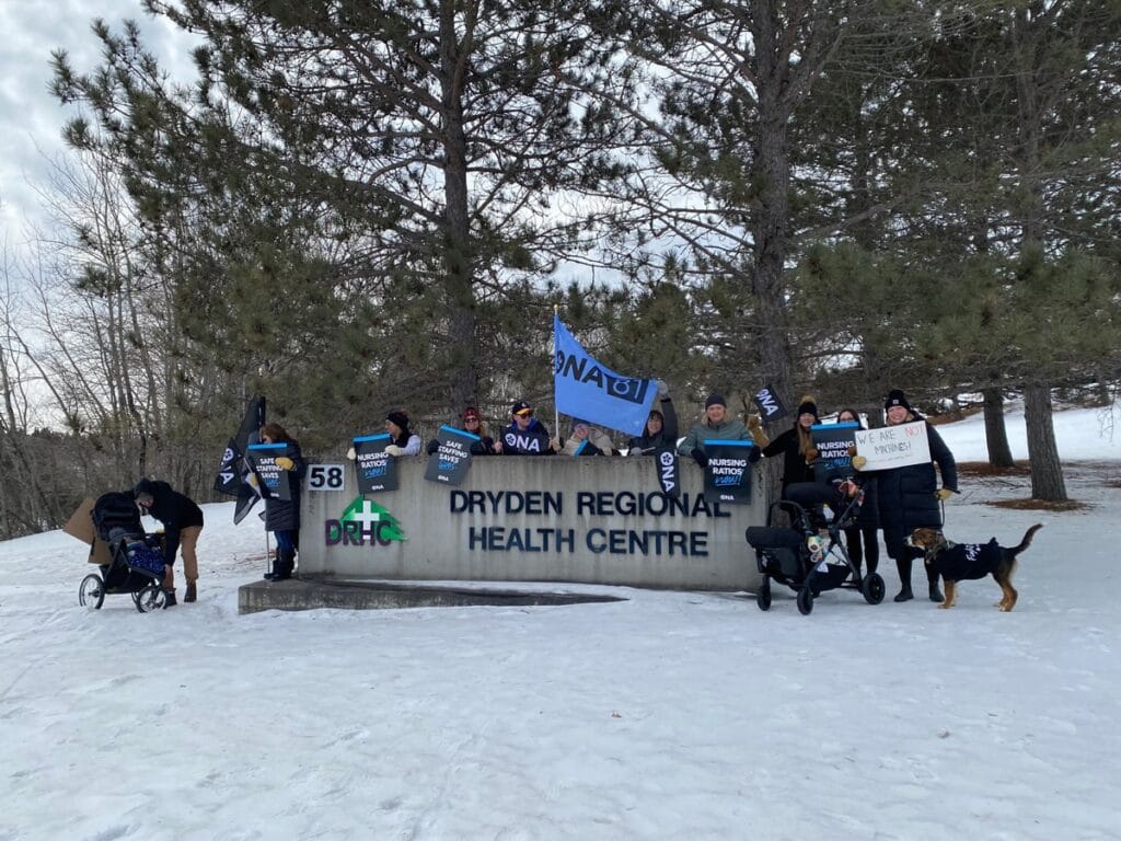 Members lean against and hang over a large outdoor hospital sign.