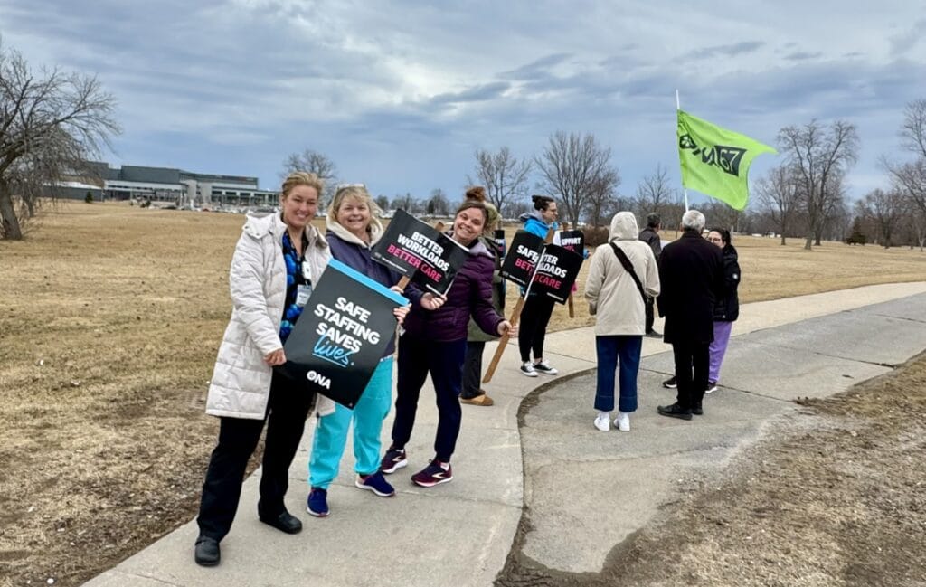 Line of members on sidewalk carry union flags with hospital in background.