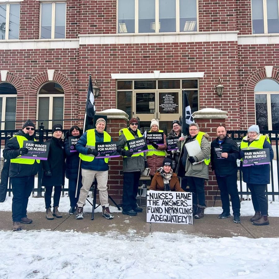 Group of members stand in a row holding signs outside MPP’s office.