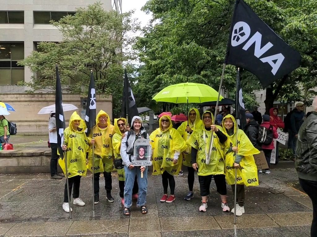 Member Hannah Stahl holds a picture of brother and is surrounded by other members at rally.