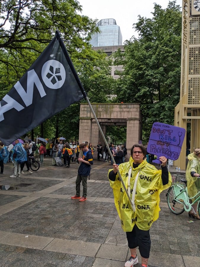 A stern looking ONA Provincial President Erin Ariss holds sign at rally.