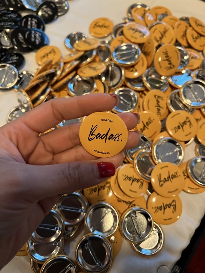 Hand is shown holding a batch of buttons reading, “badass.”