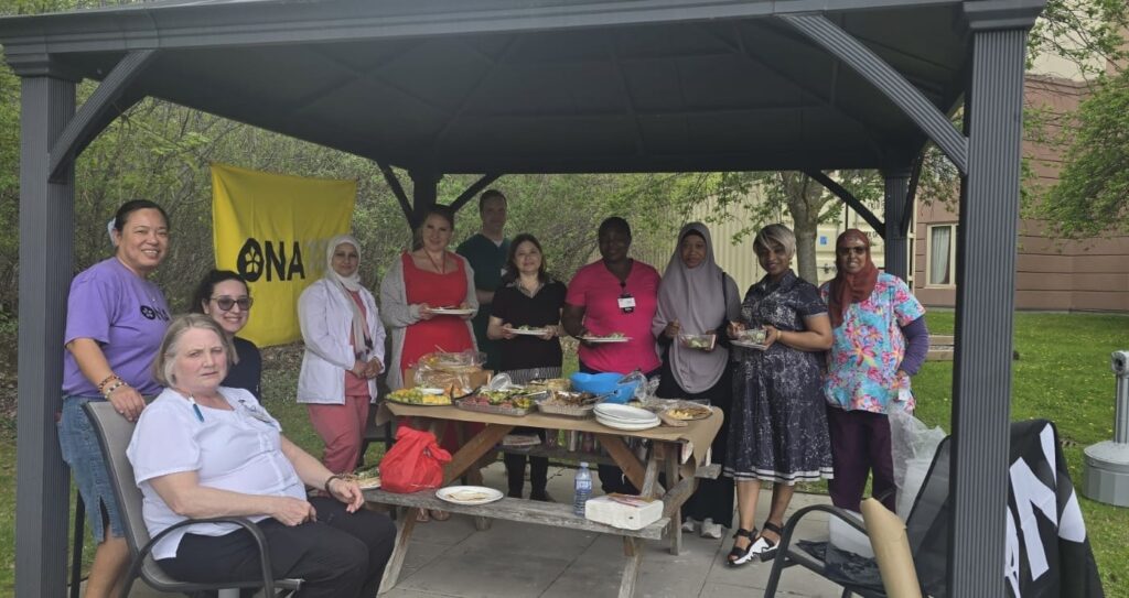 A group of people under a pergola smile for the camera while enjoying a meal together.
