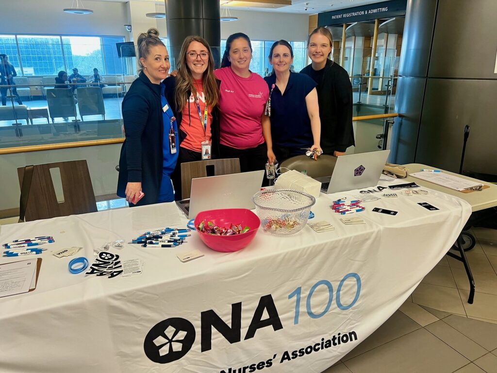 Five women pose for the camera from behind a table full of ONA materials.