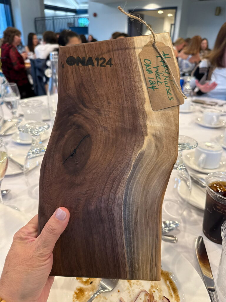 A hand holds up a wooden charcuterie board with “ONA124” branded into the wood.