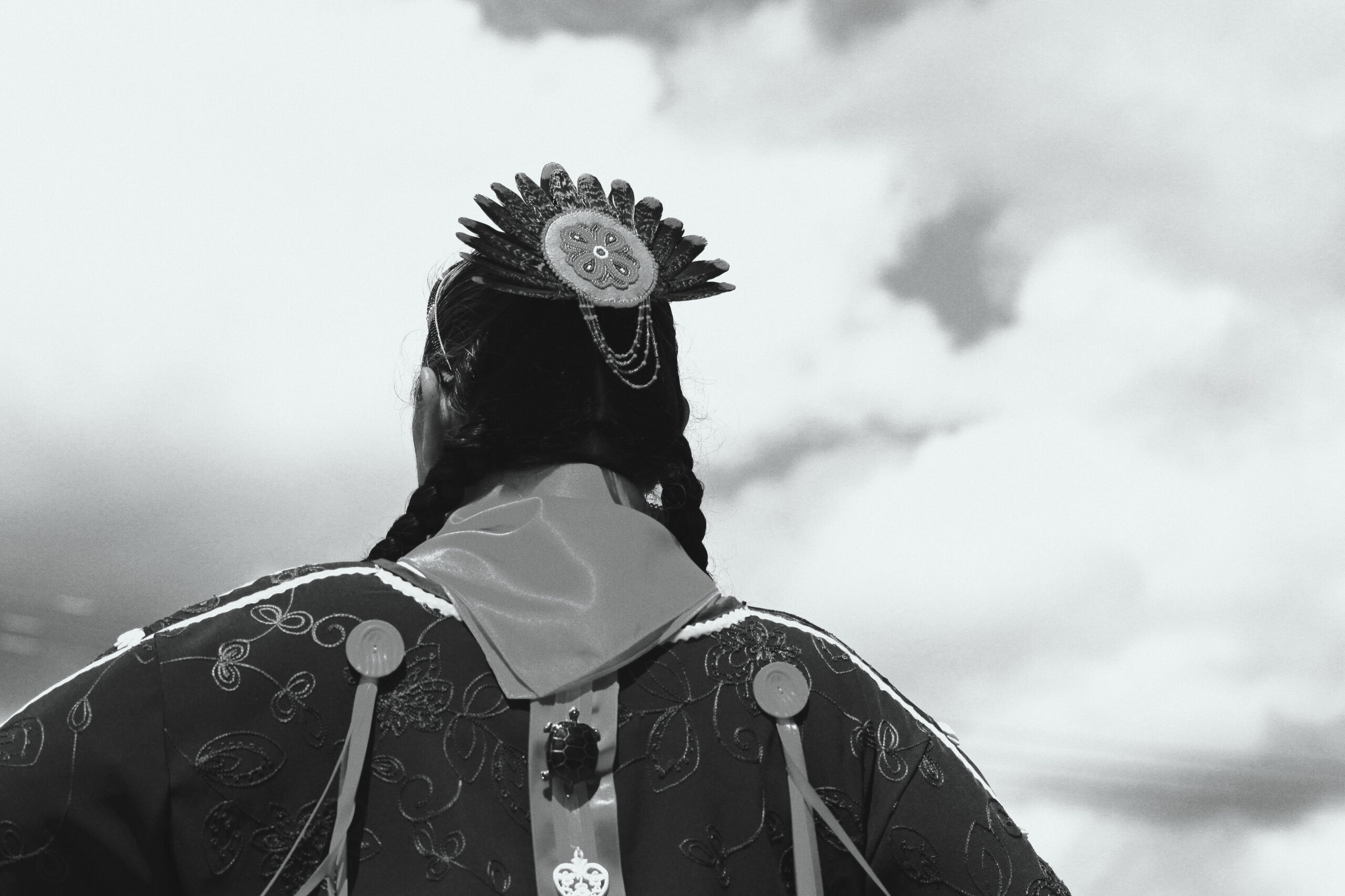A First Nations person in traditional dress stands with their back to the camera.