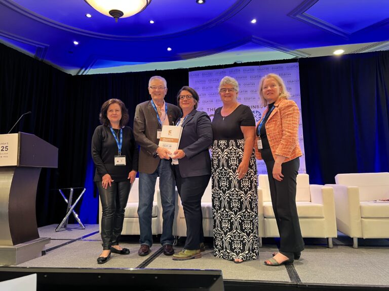 ONA President Erin Ariss is handed a program on stage, surrounded by four other people.