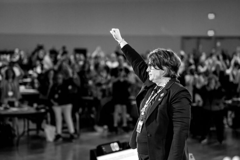 ONA Provincial President Erin Ariss stands in front of a crowd of members, raising her fist into the air.