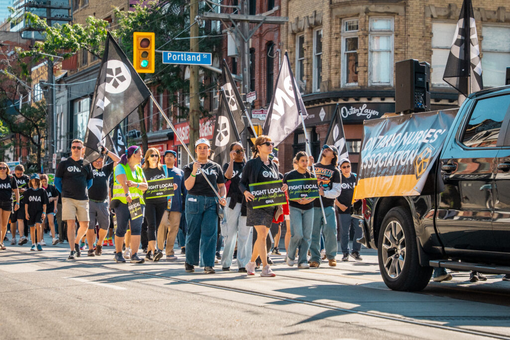 A crowd of people march down a Toronto street, holding signs.