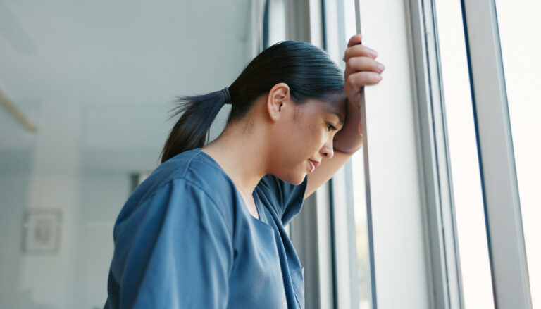 A nurse leans against a window, looking out.