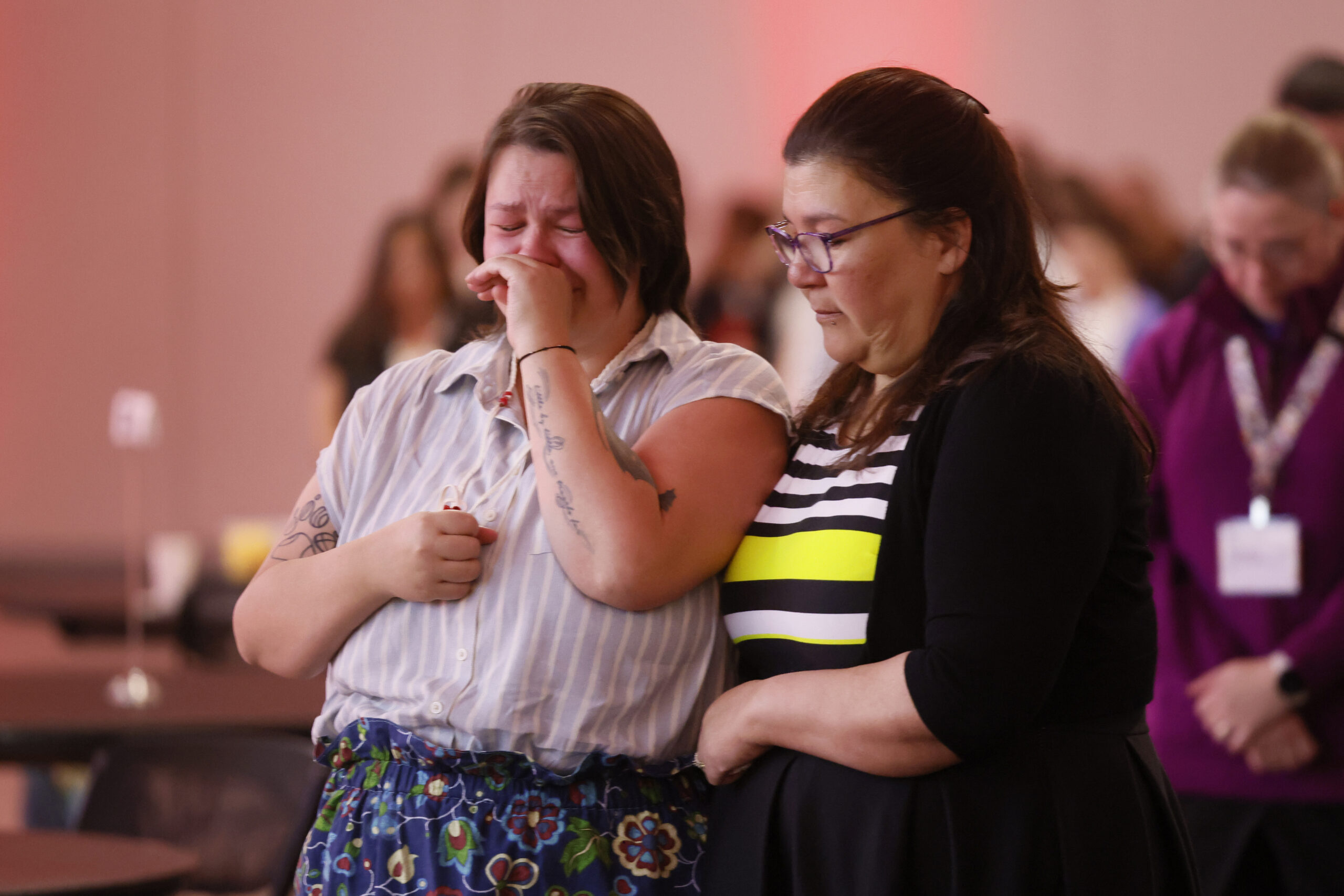 Two women stand together, arms around each other, crying.