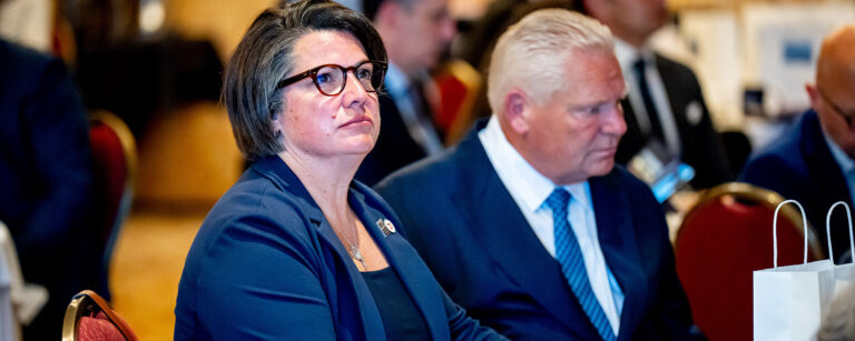 ONA President Erin Ariss looks serious sitting next to Premier Doug Ford.