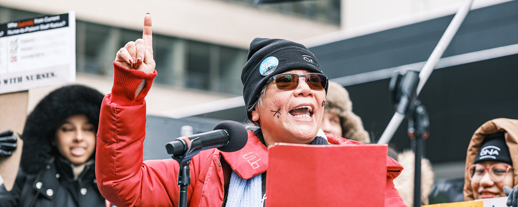 ONA member Gloria Cardinal-Tan speaks to the crowd from a stage at a rally.