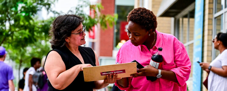 Two women on street look at a petition.