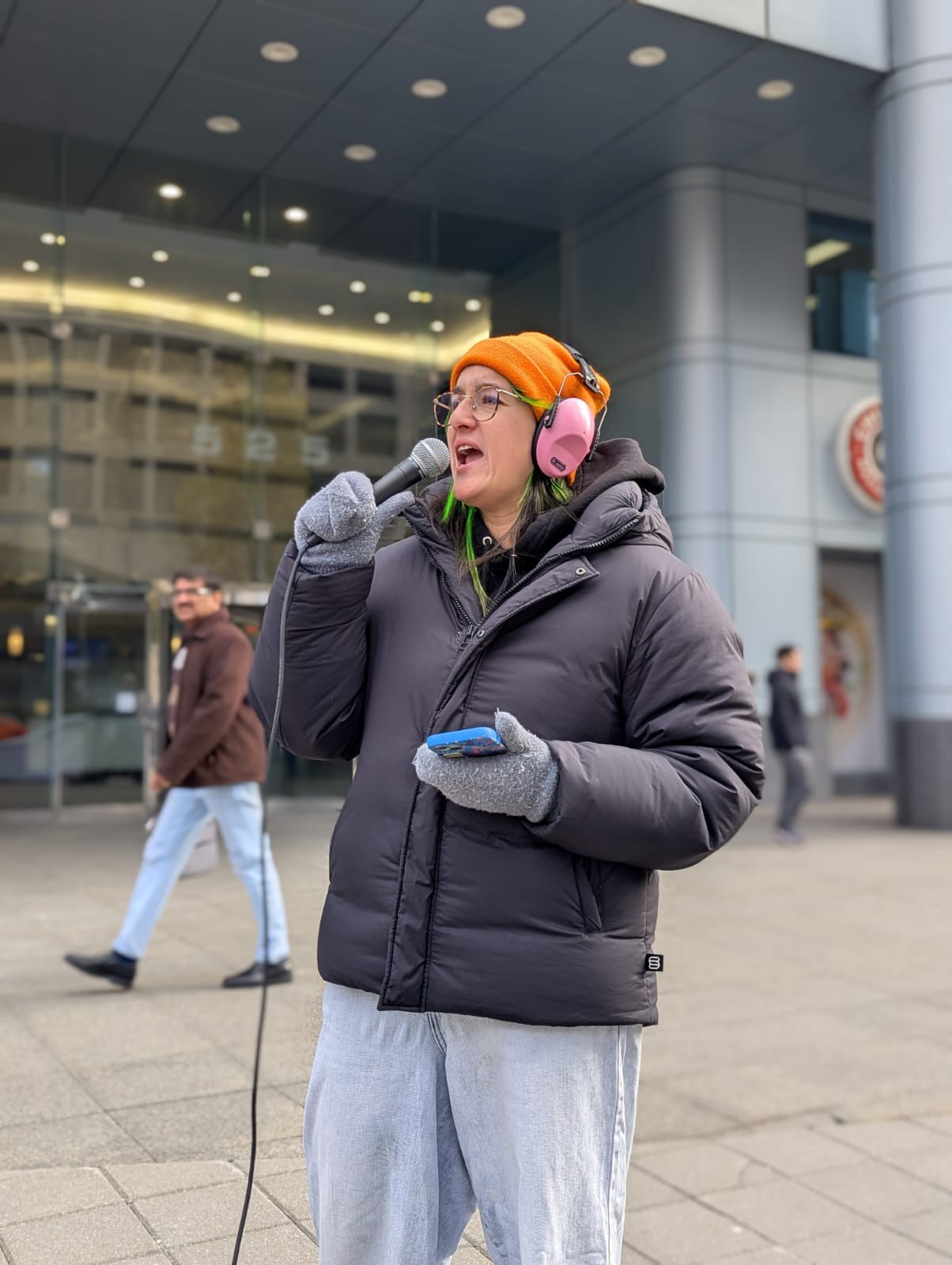 ONA member Emerald Lacaille talks into a microphone on a street.