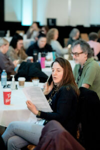Woman sitting down reads script while on phone.