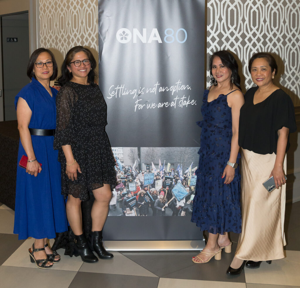Four smiling members in dresses stand in front of an ONA80 backdrop.