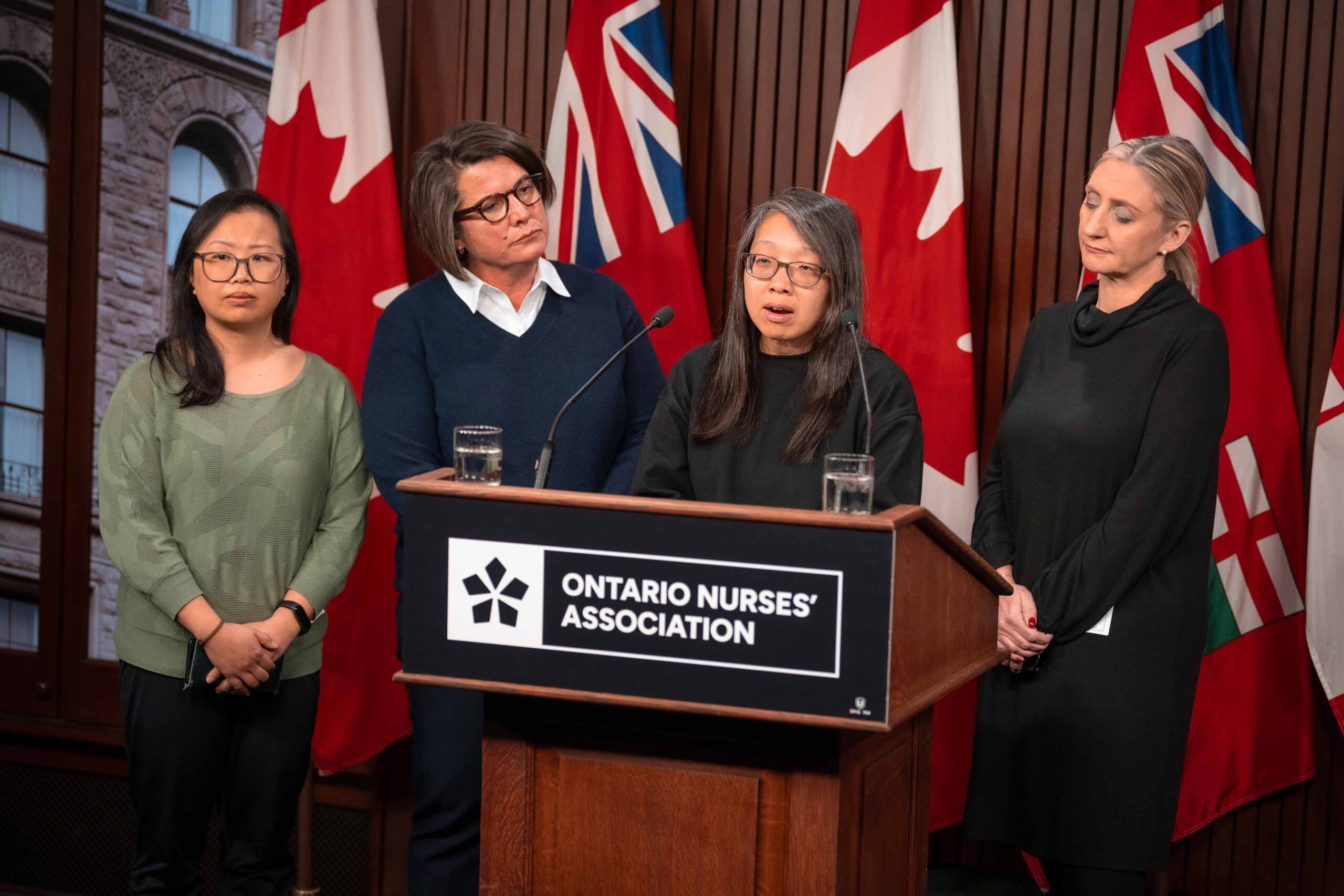 NYFHT Bargaining Unit President Rita Ha, a registered pharmacist, speaks at the podium while ONA Provincial President Erin Ariss and two others look on.