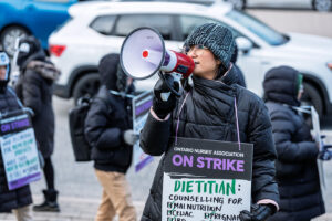 Member wearing a sign speaks into megaphone.