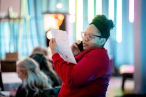 Woman standing reads script while on phone.