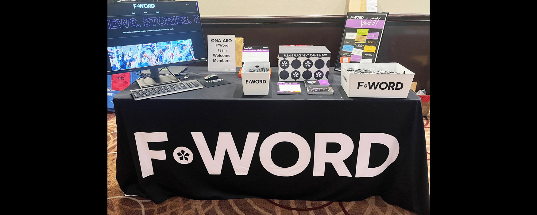 The F-Word table before the crowds displaying promotional items, a Vent box, monitor and signs.
