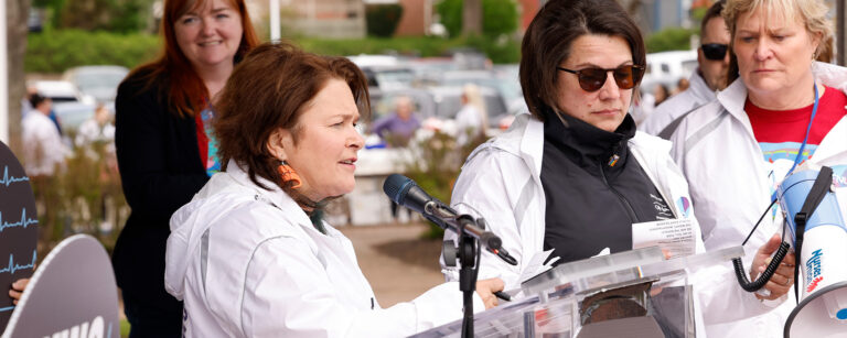 CFNU President Linda Silas stands at a podium on stage surrounding by three others.